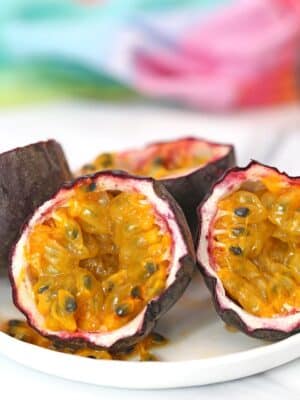 Two passion fruit, cut in half, on a white plate with a colorful napkin in the background.