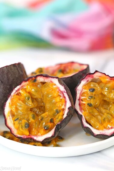 Two passion fruit, cut in half, on a white plate with a colorful napkin in the background.