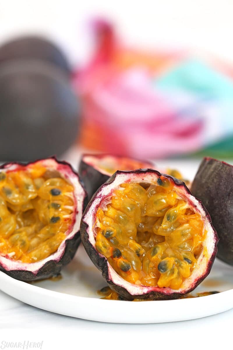 Several cut-up passion fruit on a white plate with a colorful napkin in the background.