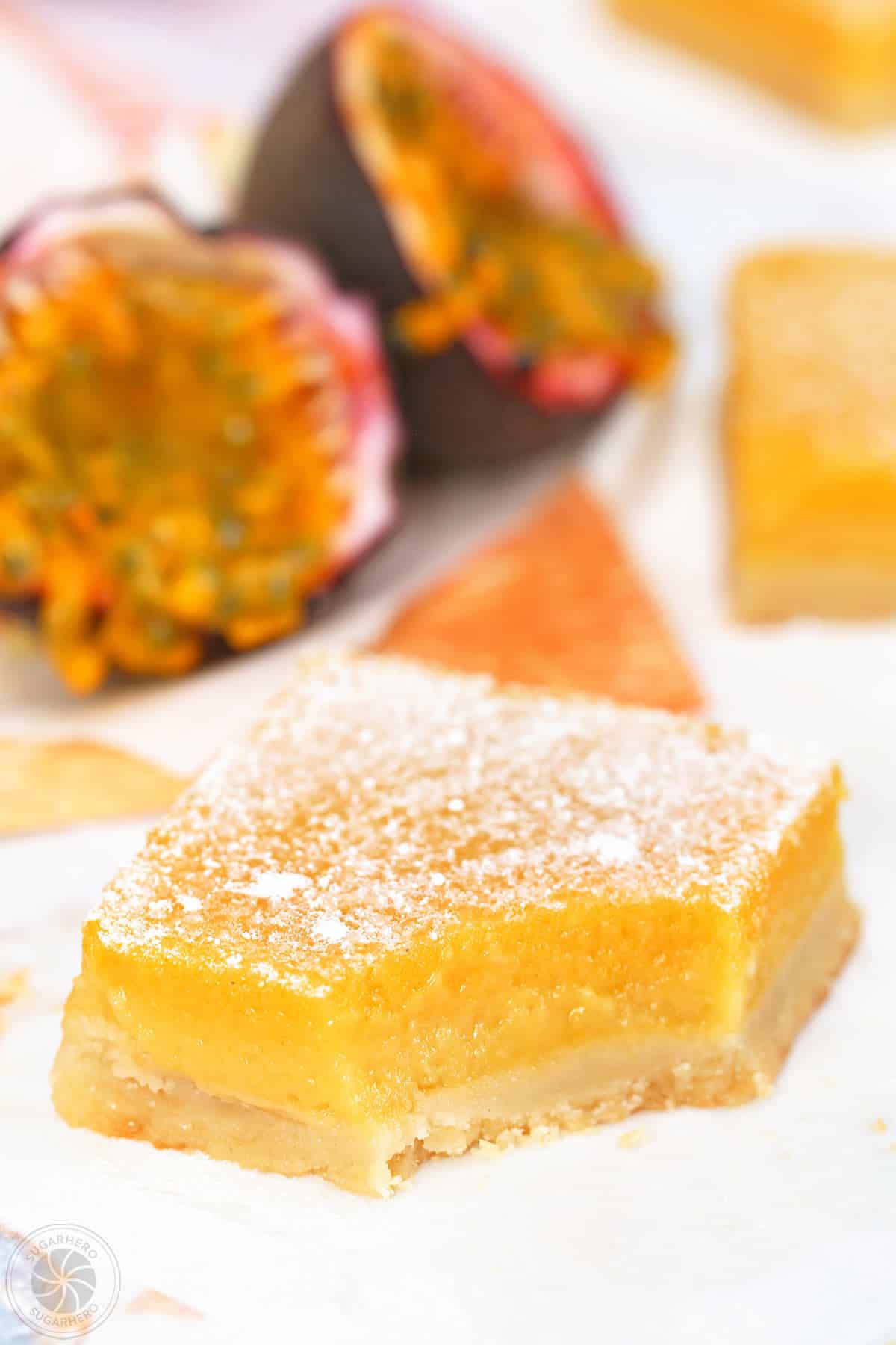 Passion Fruit Bar with bite taken out to show texture with passion fruit in the background.