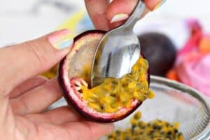 Photo of hands scraping out the filling from a passion fruit with Pinterest text overlay.