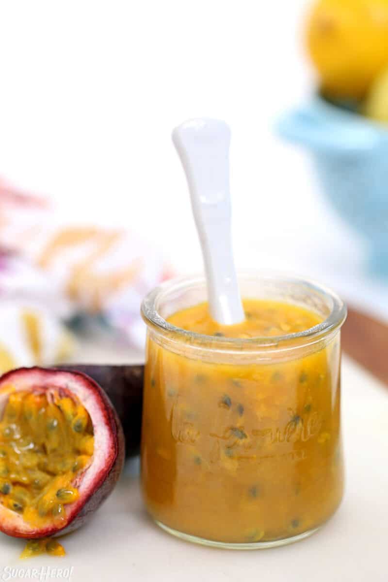 Passion fruit pulp in a small glass jar with a white spoon sticking out.