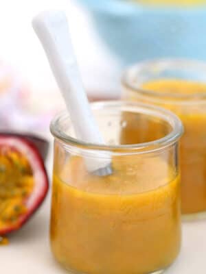 Passion fruit puree in a glass jar with a white spoon sticking out.