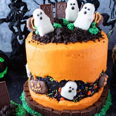 Layer cake frosted with orange buttercream, decorated with ghosts and crumbled chocolate cake to look like a graveyard.