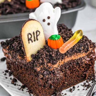 Slice of dirt cake with chocolate crumbles, a cookie headstone, and candy ghosts and pumpkins to look like a graveyard.