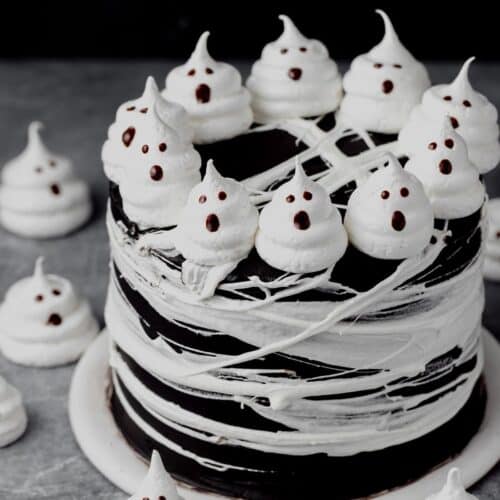 Black layer cake covered in marshmallow spiderwebs and topped with meringue ghosts.