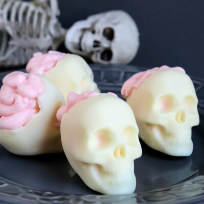 4 white chocolate skulls with pink mousse brains on a black plate.