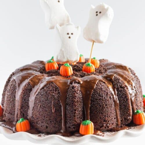 Chocolate bundt cake with chocolate drip, decorated with candy pumpkins and ghost-shaped peeps.