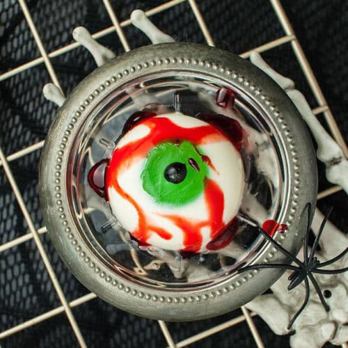 Single Halloween Panna Cotta Eyeball on a clear glass plate held by a skeletal hand.