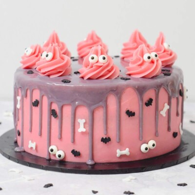 Pink layer cake with gray drips, decorated with candy eyeballs, bones, and bats.