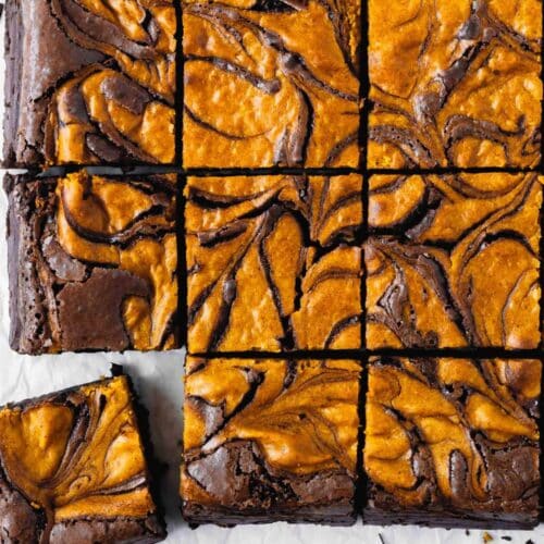 Swirled cheesecake brownies cut into squares on white parchment.