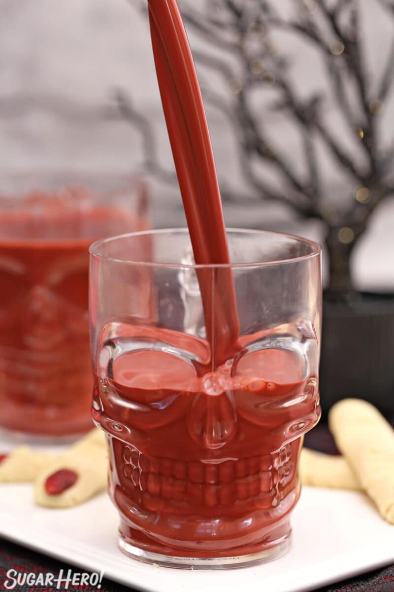 Pouring red velvet hot chocolate from above into a clear skull-shaped mug.