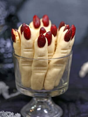 Witch Finger Cookies upright in a glass, with a skull and silver pumpkin in the background.