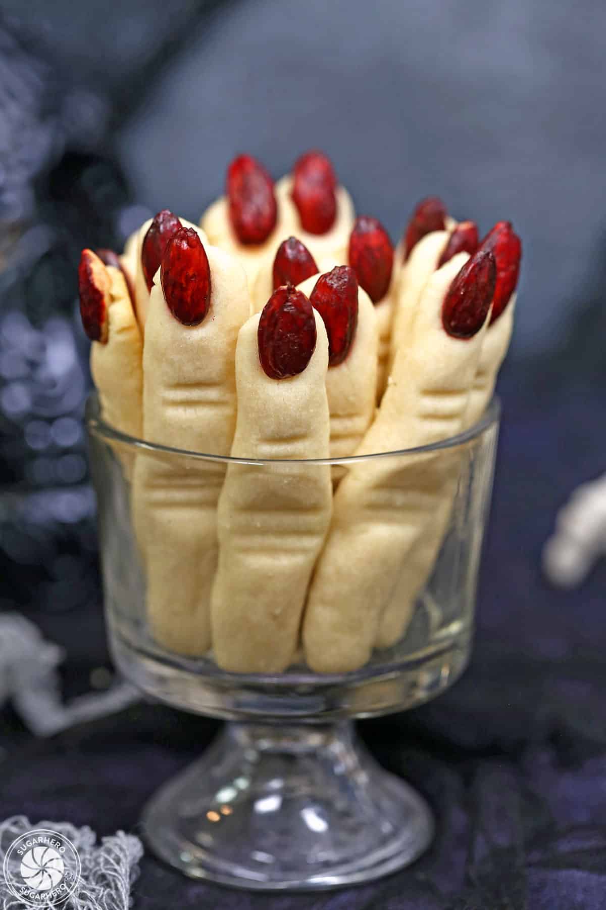 Witch Finger Cookies upright in a glass, with a skull and silver pumpkin in the background.