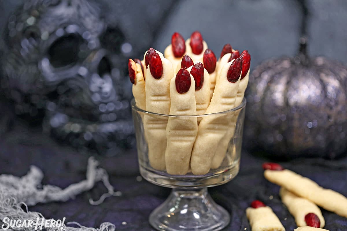 Witch Finger Cookies upright in a glass, with a skull and silver pumpkin in the background.