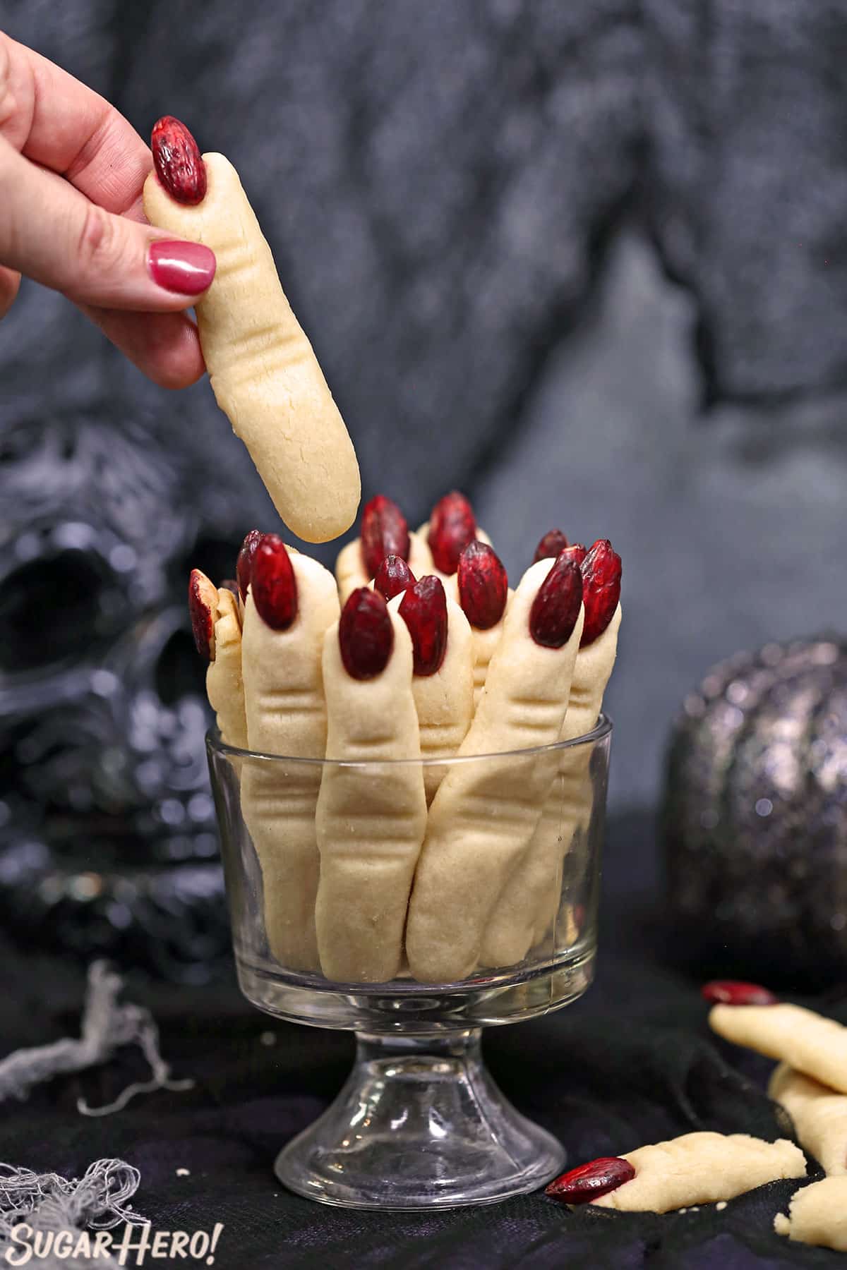 Witch Finger Cookies upright in a glass with a hand pulling one cookie out.
