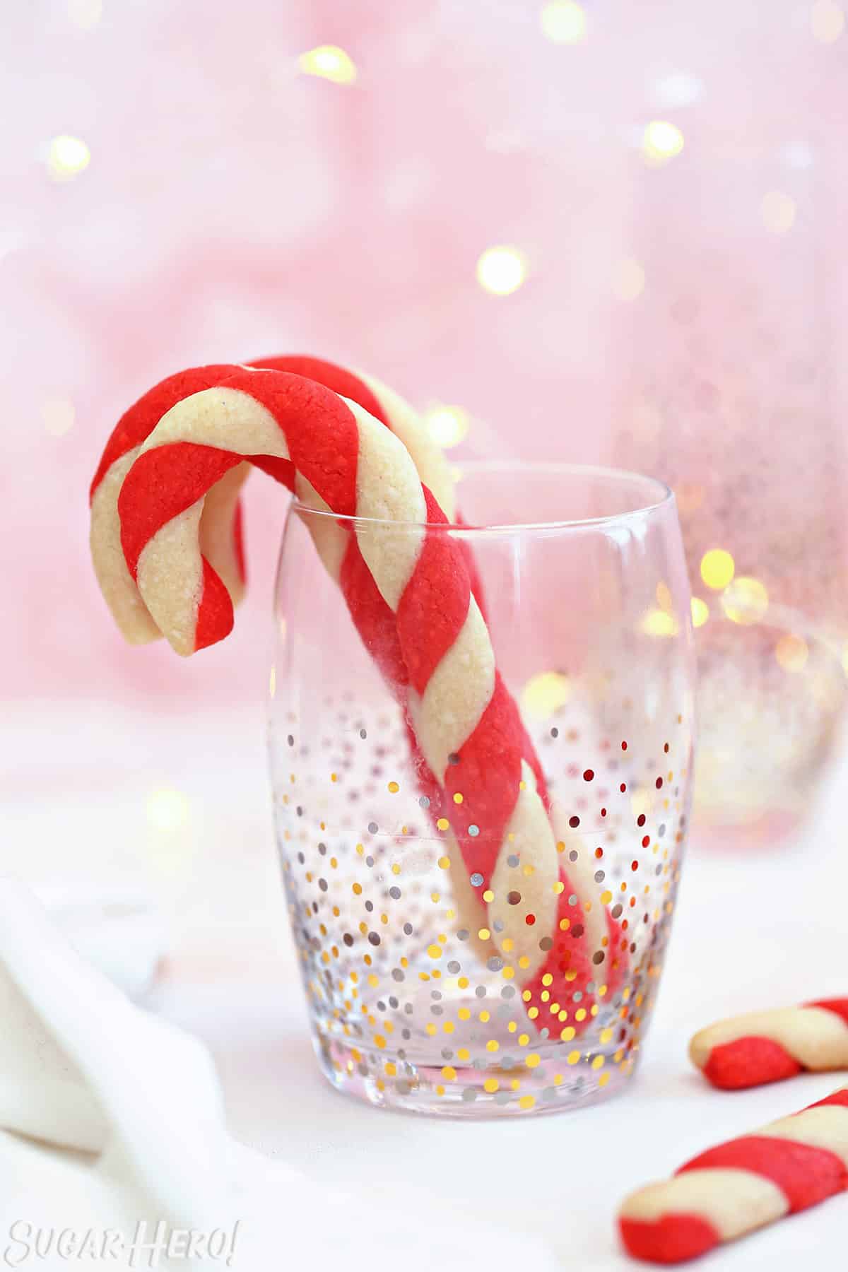 Candy Cane Cookies standing up in a clear glass with gold and silver dot accents.