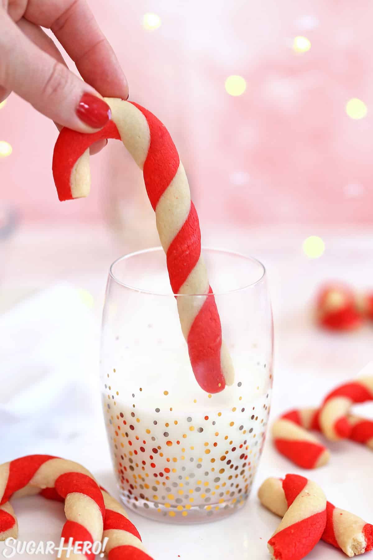 Hand about to dunk a candy cane cookie into a glass of milk.