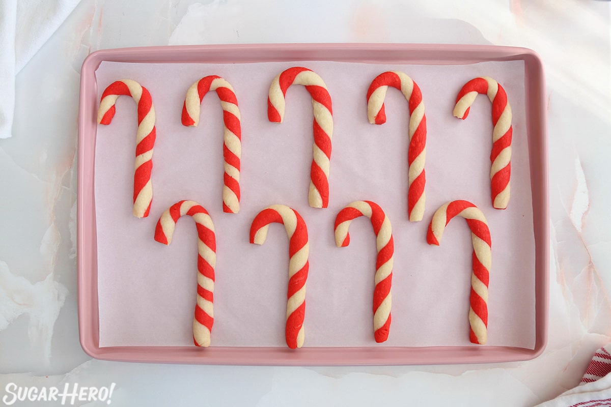 Nine Candy Cane Cookies on a parchment-covered pink baking sheet.