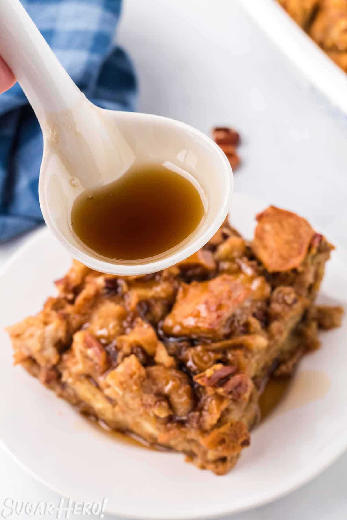 White spoon drizzling Cinnamon Syrup on top of pumpkin bread pudding.