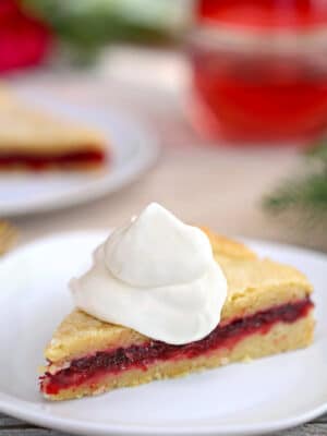Slice of Cranberry Sauce Cake on a white plate with a mound of whipped cream on top.