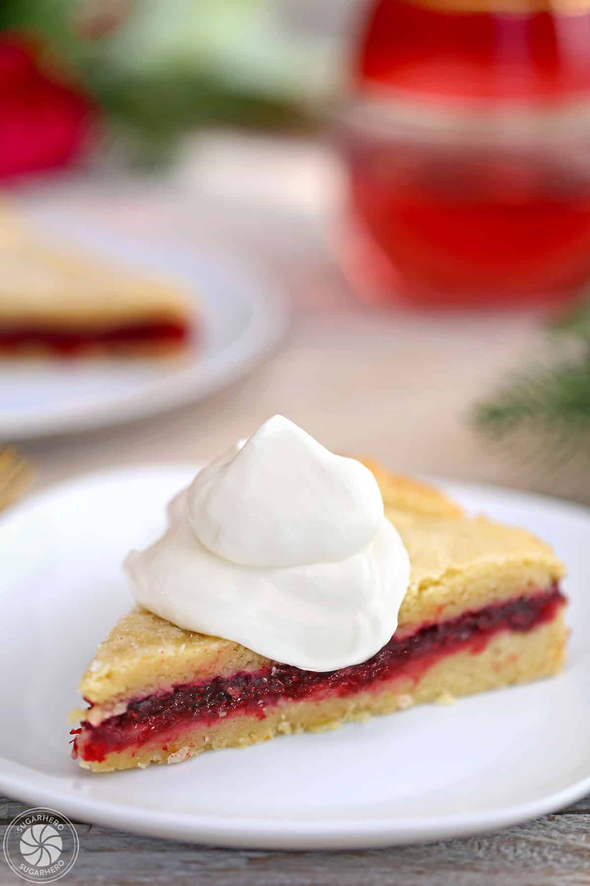 Slice of Cranberry Sauce Cake on a white plate with a mound of whipped cream on top.