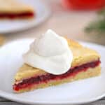 Slice of Cranberry Sauce Cake topped with whipped cream, on a white plate.