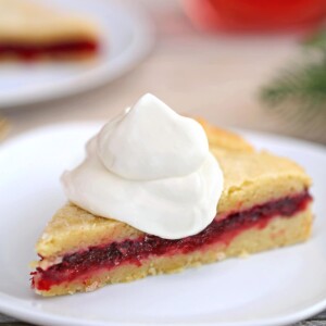 Slice of Cranberry Sauce Cake topped with whipped cream, on a white plate.