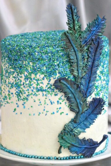 Cake with an assortment of blue and green chocolate feathers affixed to the side.