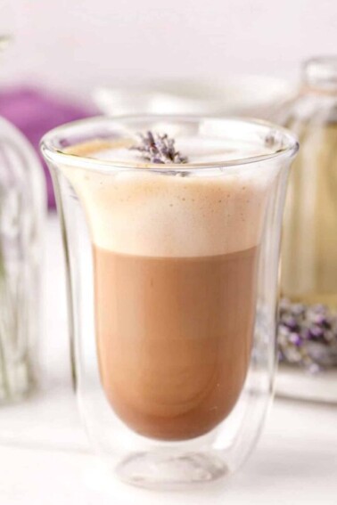 Lavender Latte in a clear glass with fresh lavender on top.