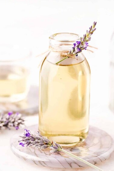 Lavender syrup in a clear glass jar, with a sprig of fresh lavender tied to the top.