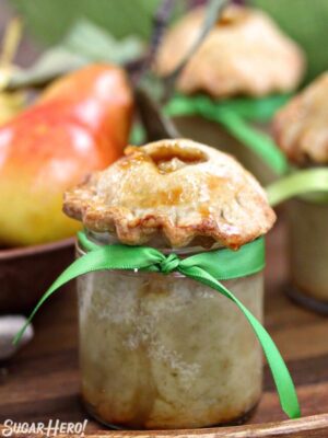 Close-up of pear pie baked in a small glass jar, with fresh pears in the background.