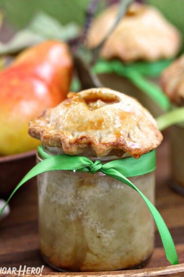 Close-up of pear pie baked in a small glass jar, with fresh pears in the background.