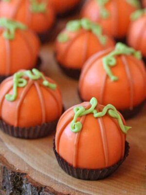 Group of truffles decorated to look like pumpkins, in brown candy cups on a wooden platter.