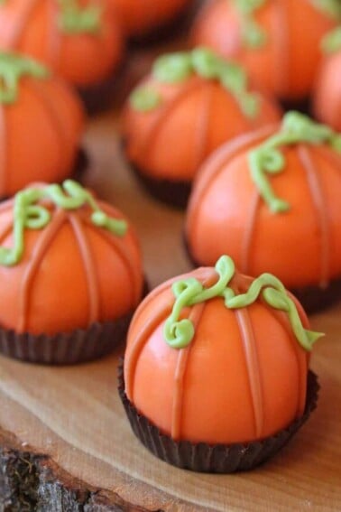 Group of truffles decorated to look like pumpkins, in brown candy cups on a wooden platter.