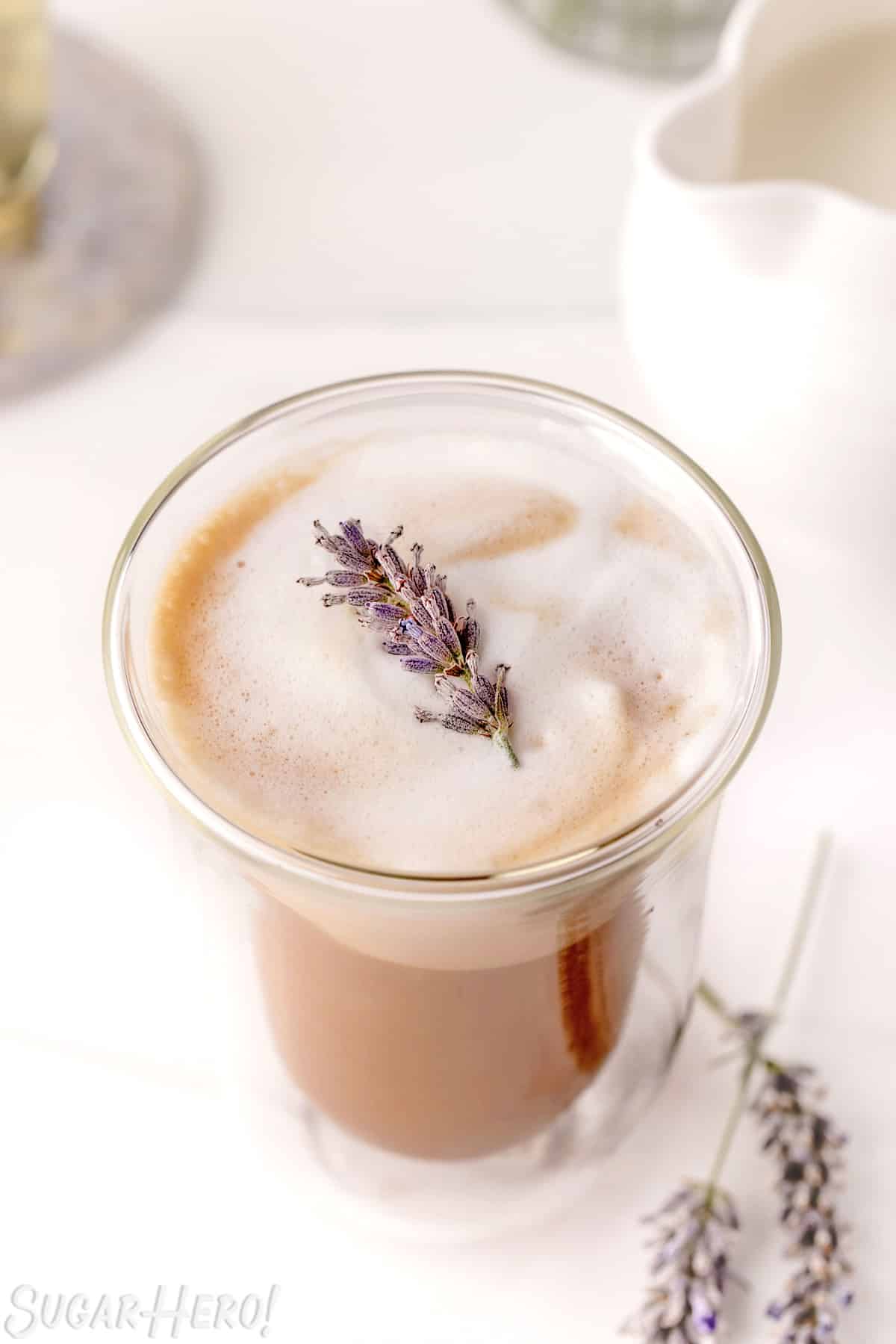 Lavender Latte in a glass with sprig of fresh lavender on top.