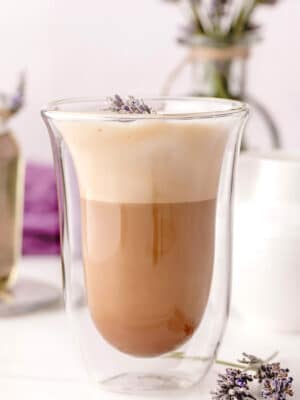 Lavender Latte in a clear glass jar with fresh lavender in the background.
