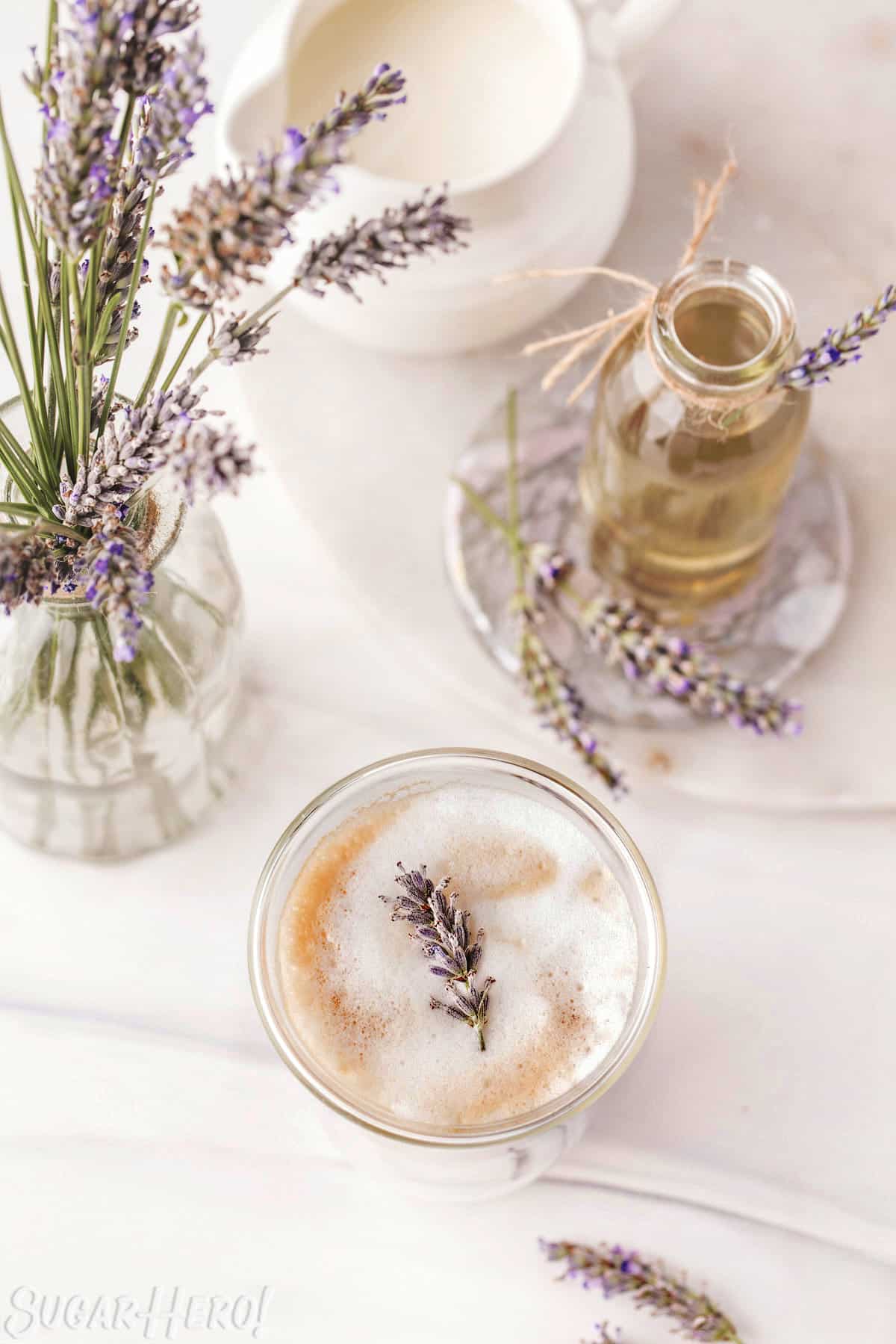 Overhead shot of a lavender latte, fresh lavender, and simple syrup in a glass jar.