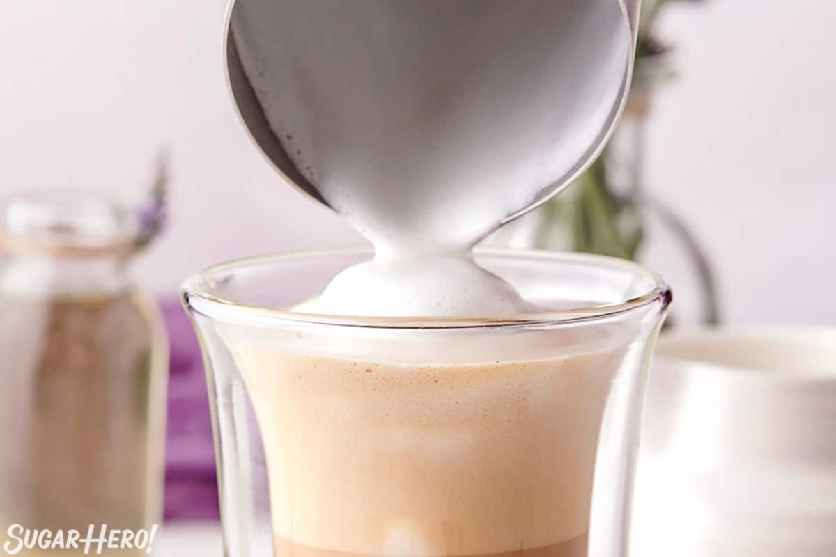Pouring steamed and frothed milk into a glass of coffee.