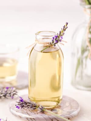 Lavender syrup in a clear glass jar, with a sprig of fresh lavender tied to the top.
