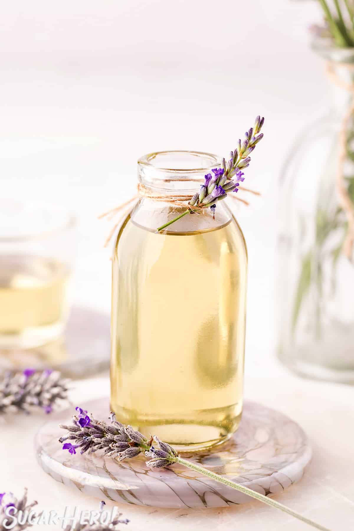 Lavender syrup in a clear glass jar, with a sprig of fresh lavender tied to the top.