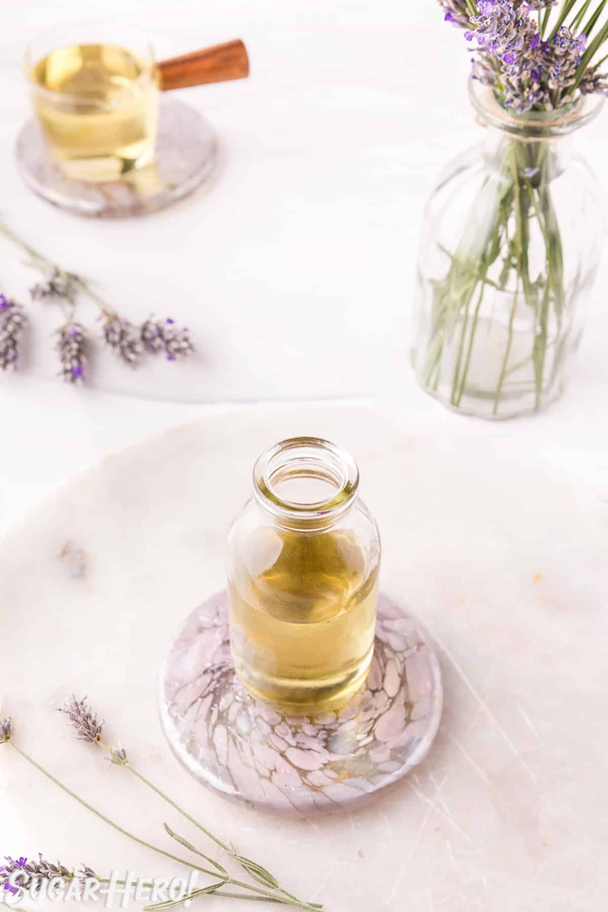 Lavender syrup in a glass jar on a marble plate, with fresh lavender scattered around.