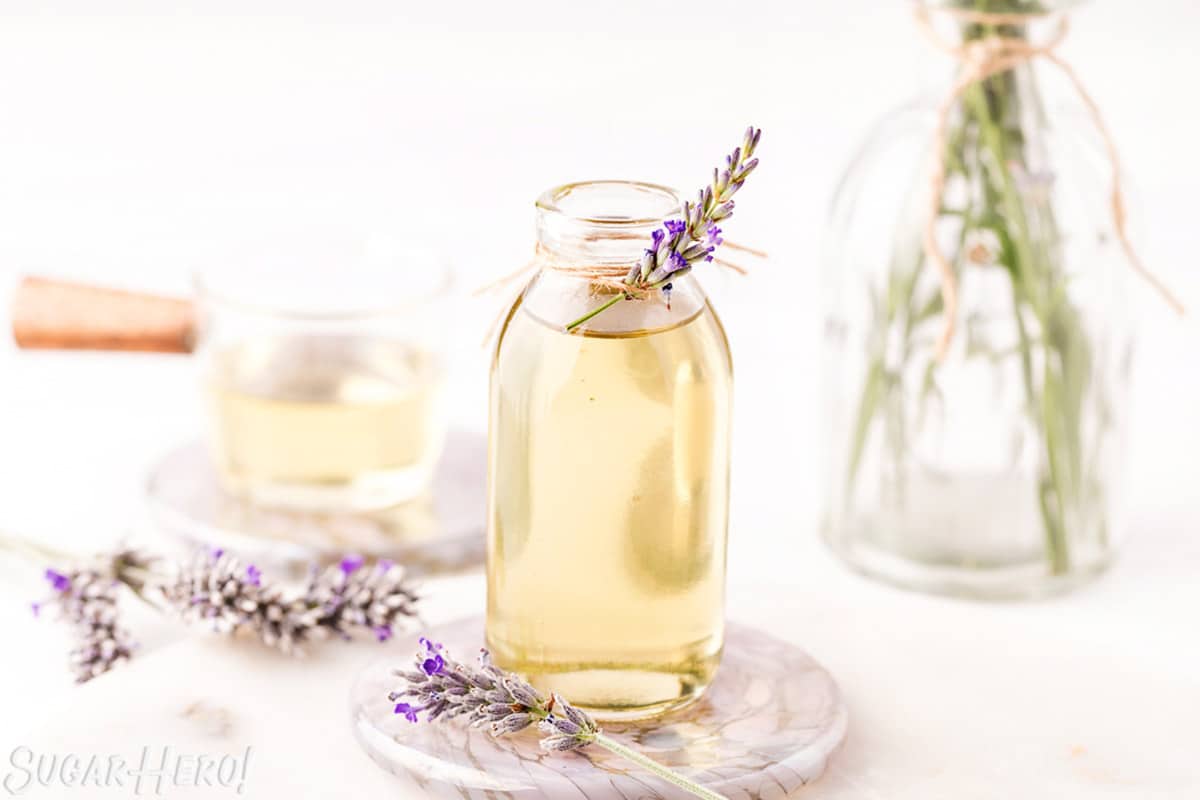 Lavender syrup in a clear glass jar, with a sprig of fresh lavender tied to the top.