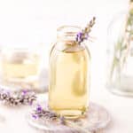 Lavender syrup in a clear glass jar, with a sprig of fresh lavender tied to the top.