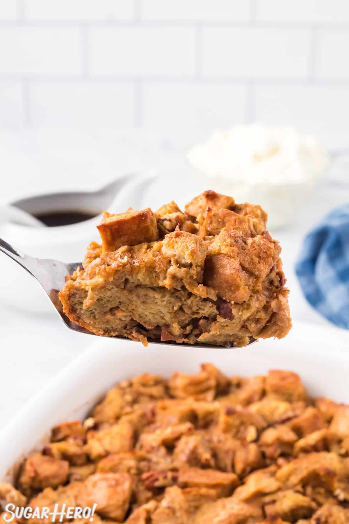 Spatula holding a slice of Pumpkin Bread Pudding over a dish of baked bread pudding.
