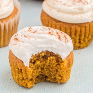 Three pumpkin spice cupcakes, the one in the front has a bite taken out of it.