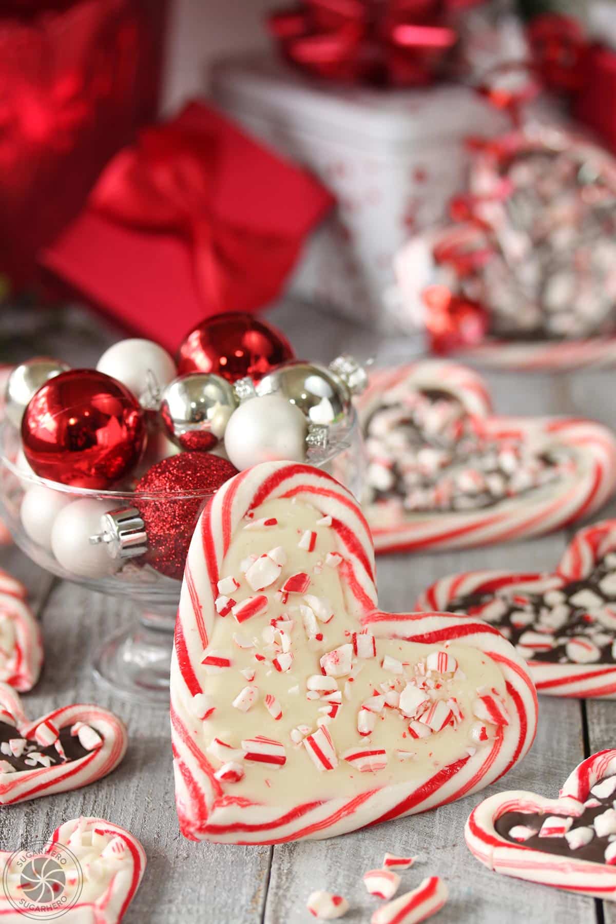 Close-up of a Candy Cane Heart with white chocolate on the inside, leaning against a glass bowl filled with shiny ornaments.