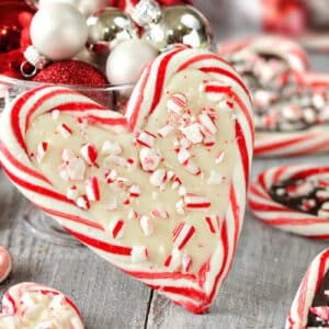 Candy Cane Heart filled with white chocolate, leaning against a glass bowl full of shiny ornaments.