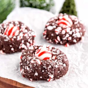 3 Chocolate Peppermint Kiss Cookies on a piece of parchment with evergreen trees in the background.