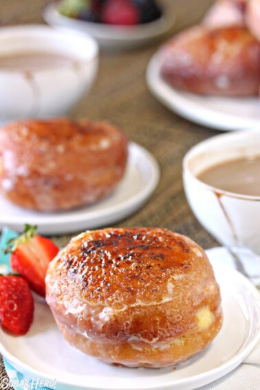 Crème Brûlée Donuts on white plates among cups of tea and fresh berries.